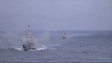 Dwa okręty wojenne płyną po morzu, jeden z nich emituje dym z tyłu.