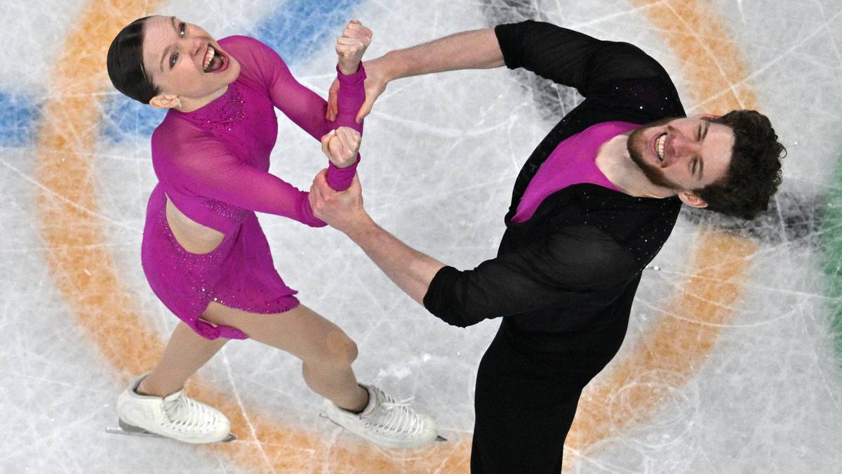 Para łyżwiarzy figurowych wykonuje układ na lodowisku, ubrani w r&oacute;żowe i czarne stroje.