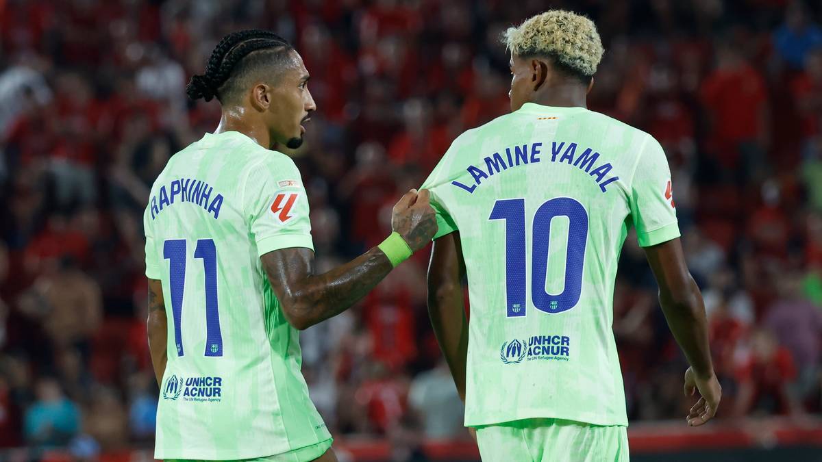 Dwóch piłkarzy FC Barcelony w jasnoniebieskich strojach stoi zwróconych do siebie. Na plecach jednego z nich widnieje nazwisko "LAMINE" i numer "10", na plecach drugiego "RAPHINHA" i numer "11". W tle widownia.