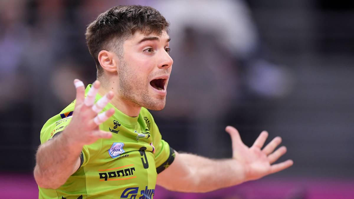 Młody mężczyzna w koszulce sportowej z otwartymi ustami i wyciągniętymi rękami.