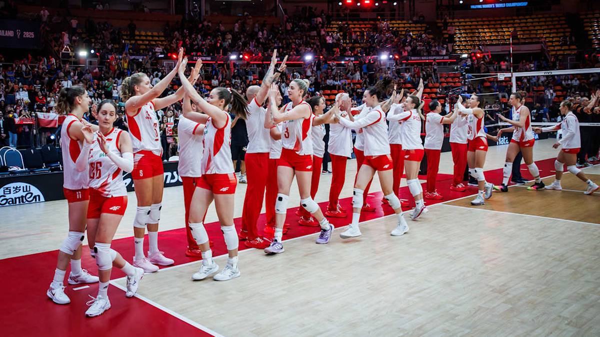 Drużyna siatkarek w białych strojach z czerwonymi elementami świętuje na boisku, unosząc ręce w górę.
