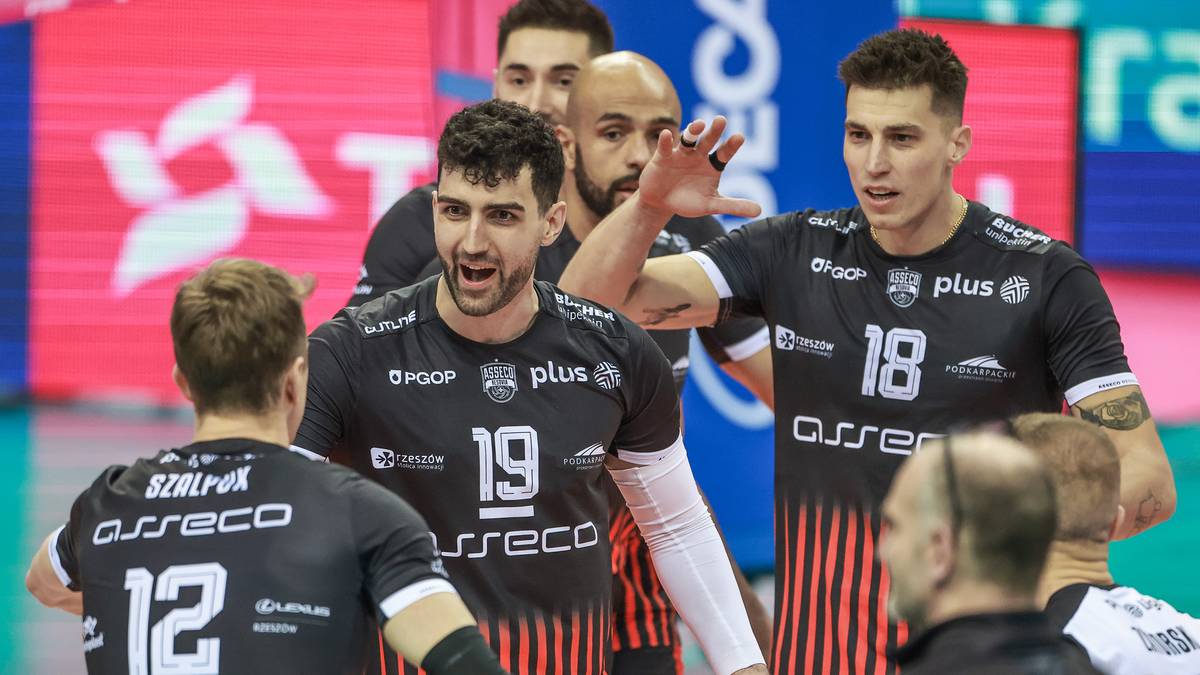 Grupa siatkarzy w czarnych strojach z numerami na koszulkach, jeden z nich udziela wskaz&oacute;wek pozostałym.