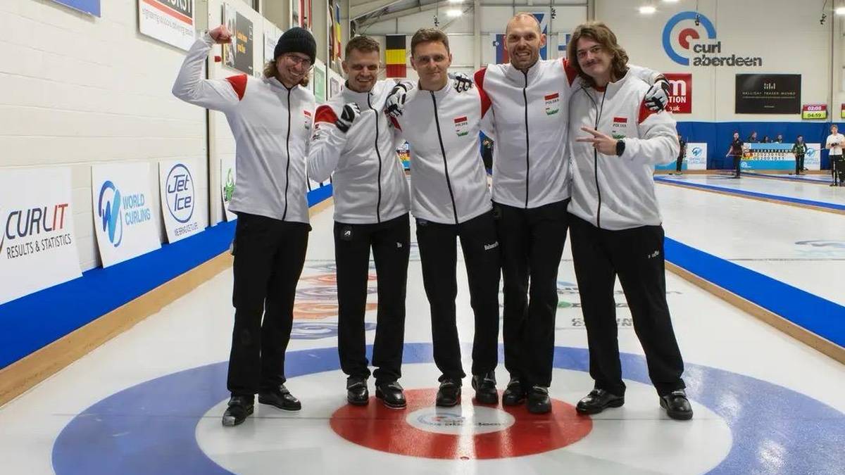 Pięciu młodych mężczyzn w strojach sportowych pozuje do zdjęcia na lodowisku do curlingu, świętując sukces.