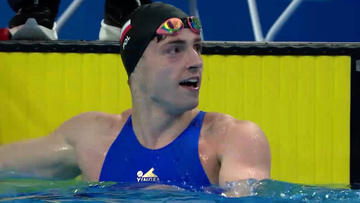 Pływak w stroju kąpielowym i czepku z okularami pływackimi na głowie w wodzie, z otwartymi ustami.