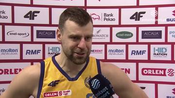 Kamil Łączyński, zawodnik koszyk&oacute;wki, udziela wywiadu przed ścianką z logo sponsor&oacute;w.