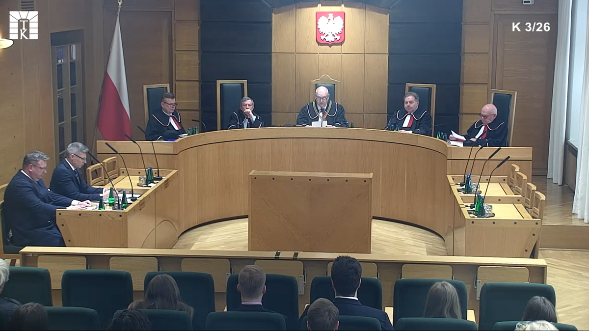 Pięciu sędzi&oacute;w w togach siedzi za stołem w sali rozpraw Trybunału Konstytucyjnego.