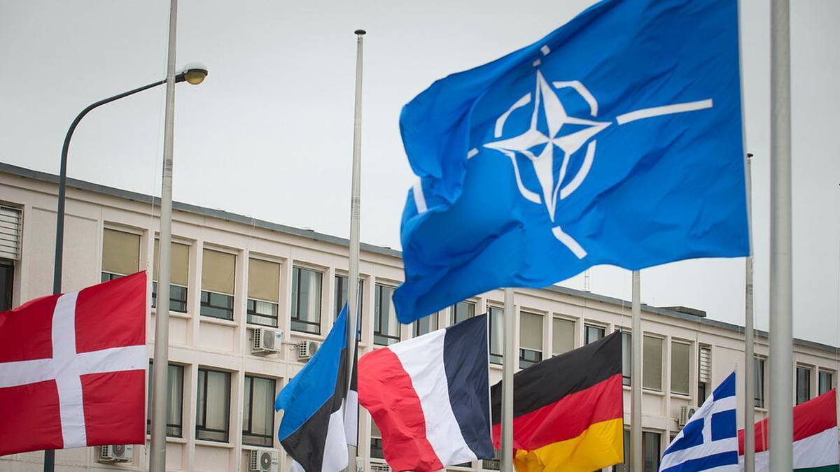 Flaga NATO na wietrze na tle budynku z innymi flagami państwowymi.