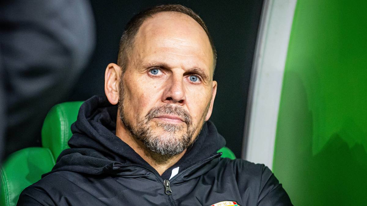 Portret trenera Simundzy siedzącego na ławce trenerskiej.