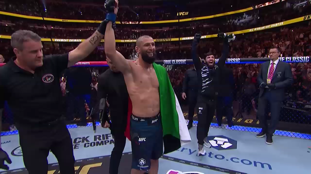 Zawodnik MMA, otoczony przez innych ludzi, wznosi ramiona do góry trzymając flagę w kolorach zielonym, białym i czerwonym, celebrując zwycięstwo na ringu UFC.