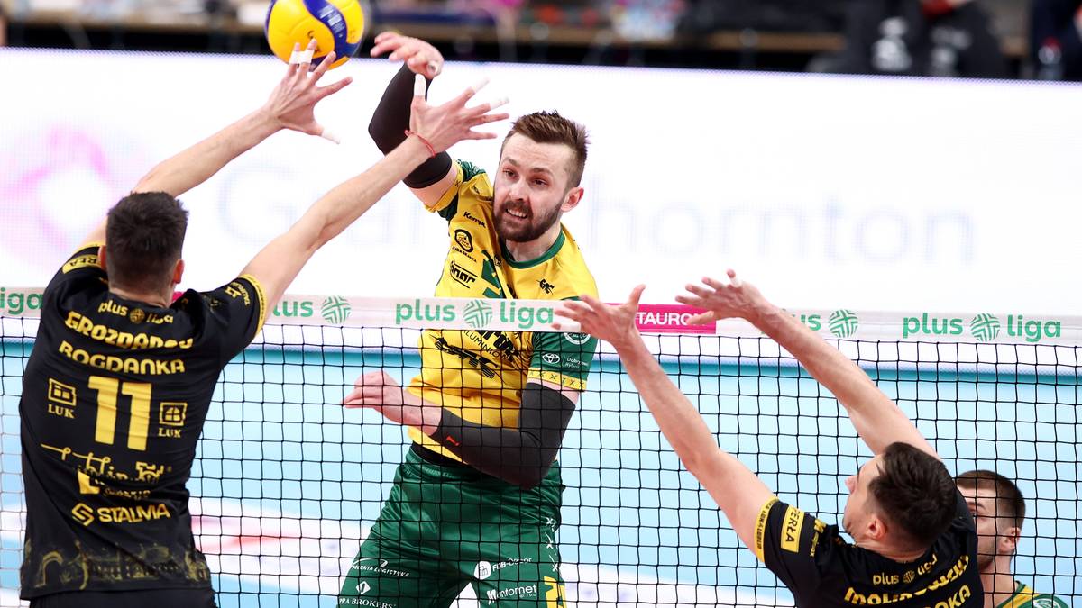 Dwóch siatkarzy blukuje atak, jeden gracz stara się odbić piłkę, która zmierza w kierunku siatki.