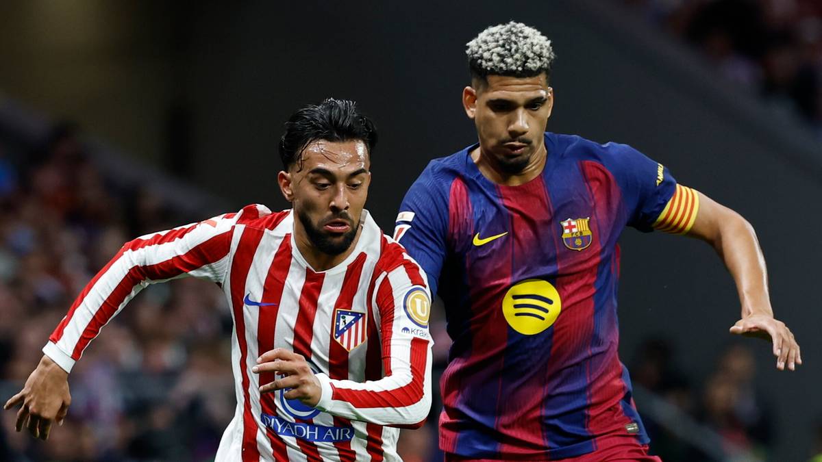 Dw&oacute;ch piłkarzy w akcji na boisku, jeden w stroju Atletico Madryt, drugi w stroju FC Barcelony, walczą o piłkę.