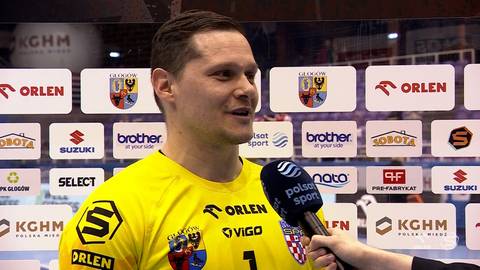 Mężczyzna w ż&oacute;łtej koszulce sportowej z numerem 1 udziela wywiadu przed ścianą z logo sponsor&oacute;w.