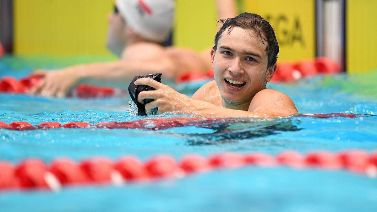 Uśmiechnięty młody pływak w basenie trzymający czepki.