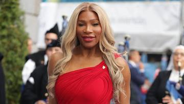Serena Williams w czerwonej sukni stoi na niebieskim dywanie
