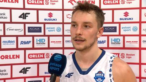 Mężczyzna w białej koszulce sportowej z logo "MKS" udziela wywiadu przed ścianą z logotypami sponsor&oacute;w.