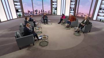 Grupa osób siedzi w okręgu w studiu telewizyjnym, uczestnicząc w dyskusji.