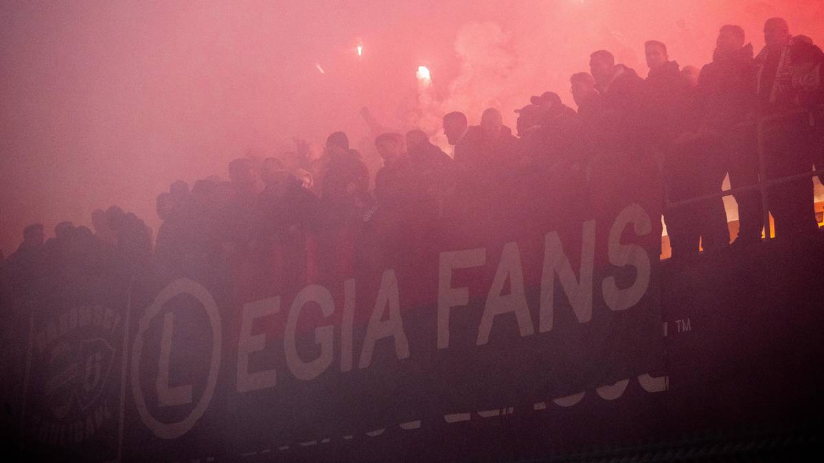 Sylwetki kibiców Legii na tle dymu i rac z napisem "LEGIA FANS"