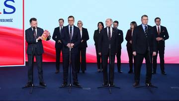 Grupa mężczyzn w garniturach stoi na scenie przed logo partii PiS.
