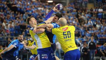 Piłkarze ręczni walczą o piłkę w trakcie meczu na pełnej trybunie.