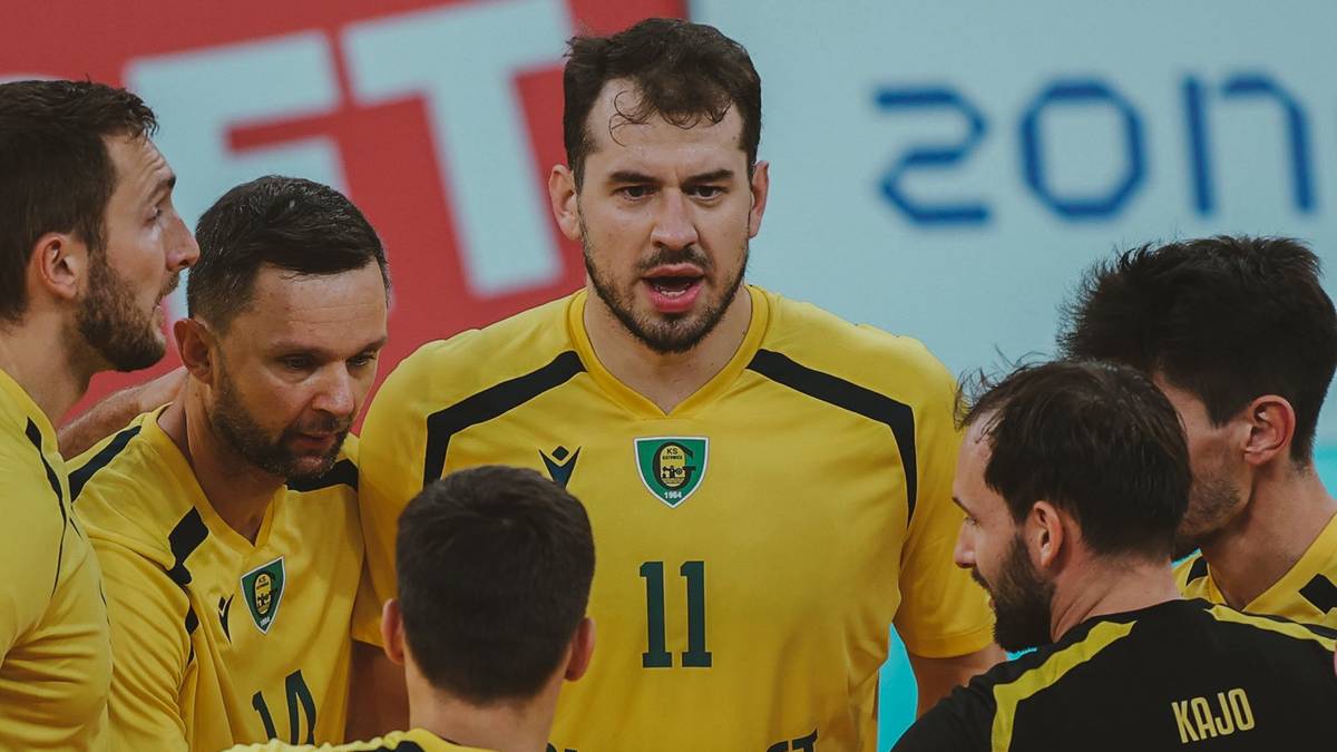 Grupa siatkarzy w żółtych koszulkach otacza swojego kolegę z numerem 11 na koszulce, wszyscy skupieni i w geście jedności.