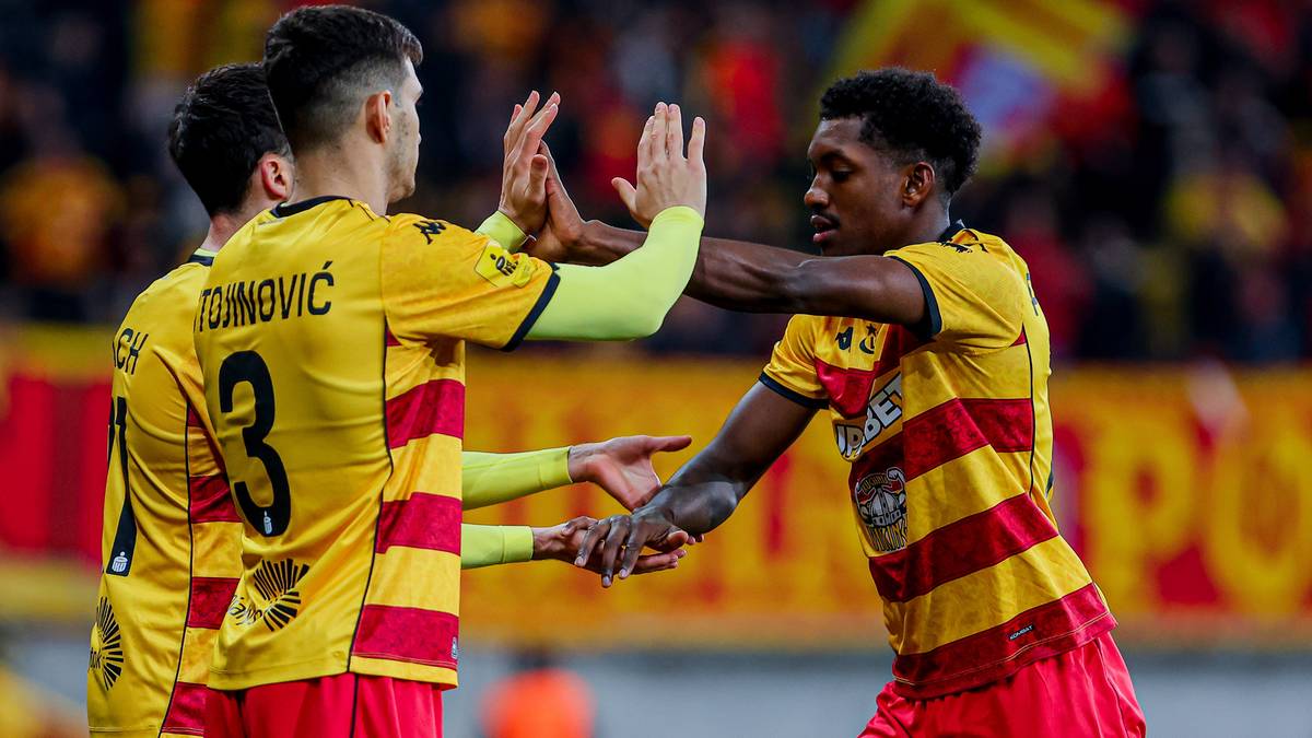 Piłkarze Jagiellonii Białystok w ż&oacute;łto-czerwonych strojach świętują razem na boisku piłkarskim.