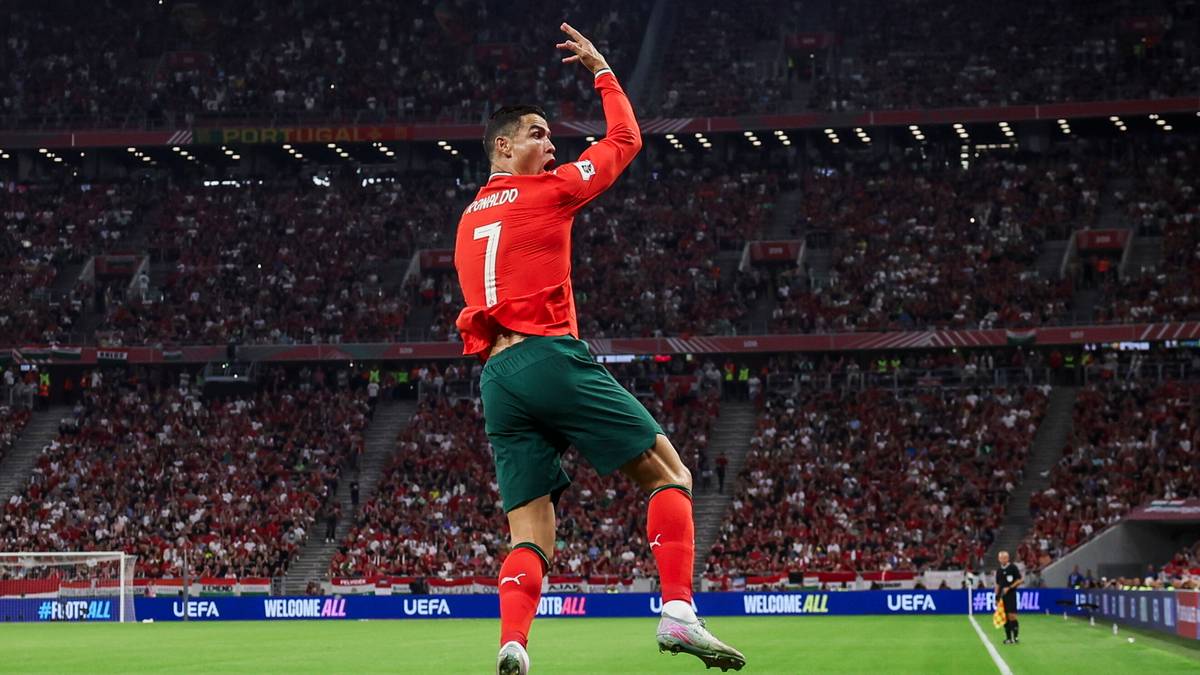 Piłkarz Cristiano Ronaldo w czerwonej koszulce z numerem 7, świętujący strzelenie gola na tle pełnych trybun stadionu.