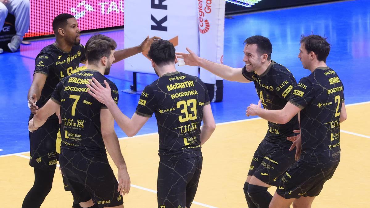 Sześciu siatkarzy w czarnych strojach z ż&oacute;łtymi numerami świętuje zwycięstwo na boisku.