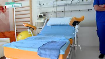 Sala porodowa ze specjalistycznym łóżkiem, piłką gimnastyczną i sprzętem medycznym w tle.