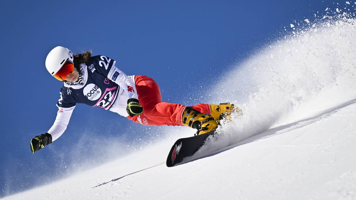 Kobieta na snowboardzie, pochylona w zakręcie, z unoszącym się śniegiem.