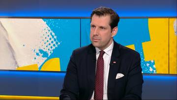 Mężczyzna w garniturze siedzi przed ekranem telewizyjnym z abstrakcyjnym wzorem w tle.