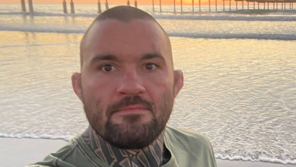 Michał Materla pozuje do selfie na plaży na tle zachodzącego słońca i molo.