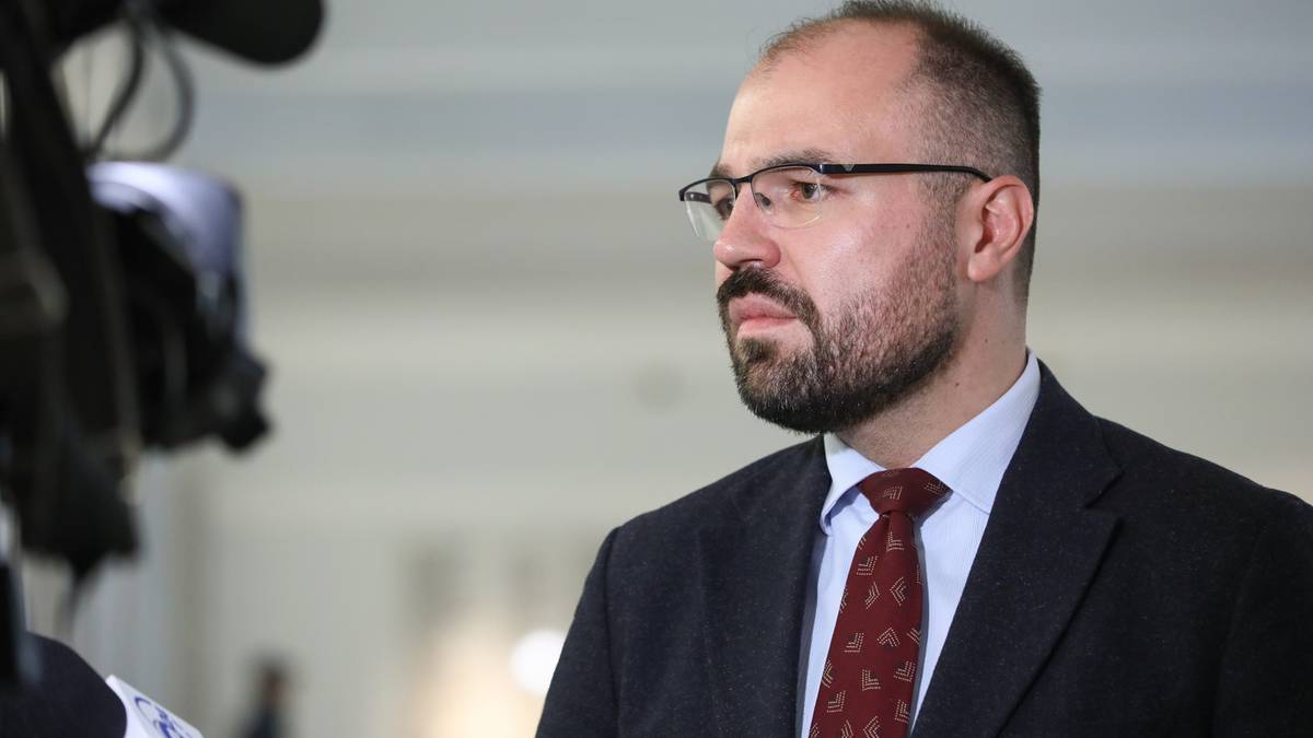 Portret Krzysztofa Szczuckiego, mężczyzny z zarostem i okularami, patrzącego w bok.