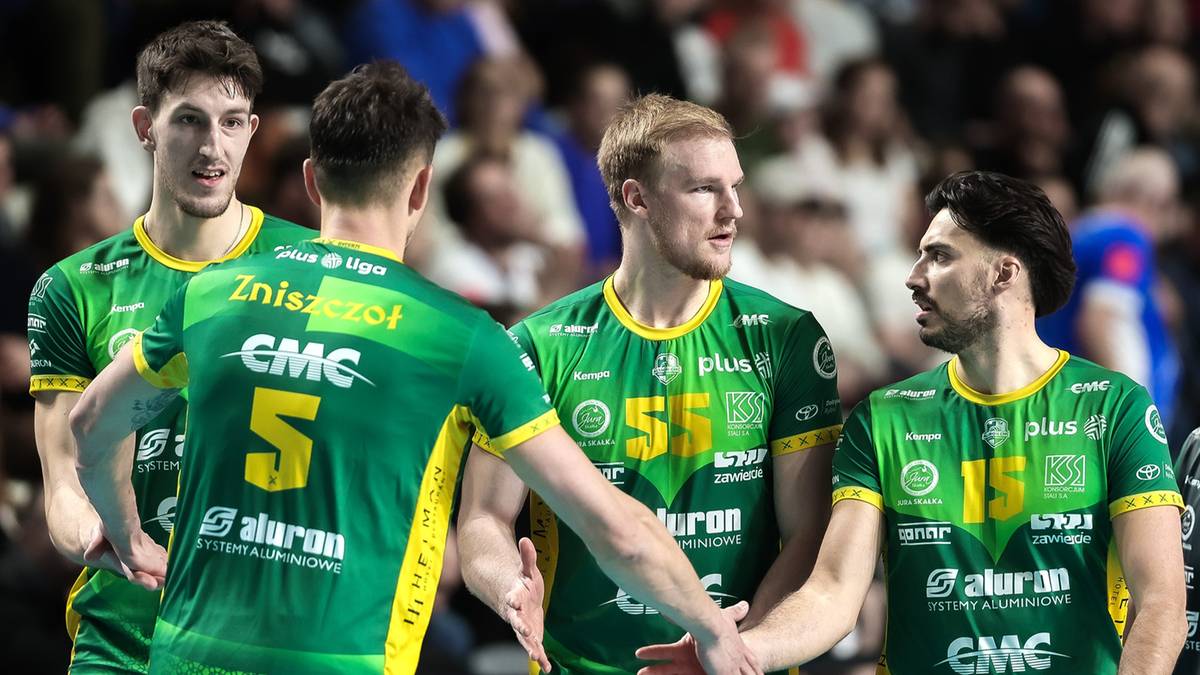 Czterech siatkarzy w zielonych koszulkach z numerami i nazwami sponsorów, dyskutujących na boisku.