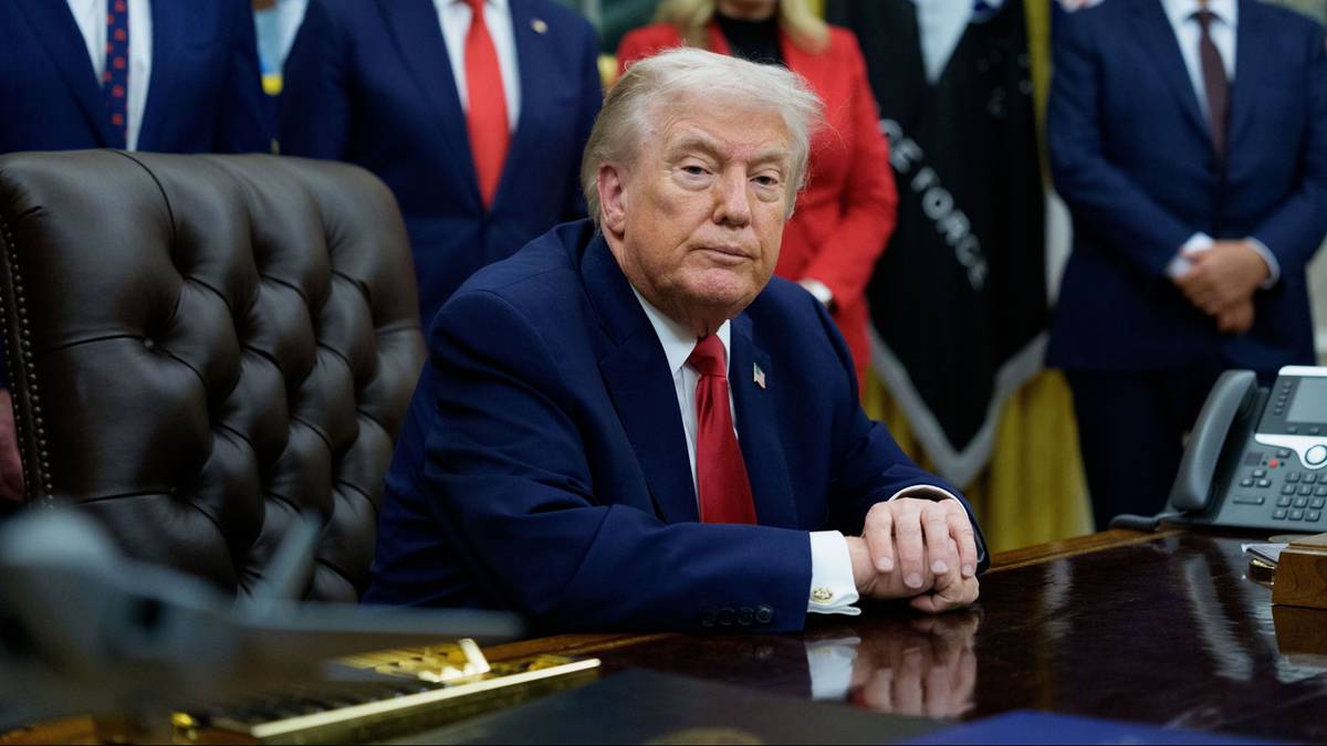 Prezydent USA Donald Trump siedzi przy biurku w Gabinecie Owalnym, otoczony doradcami.