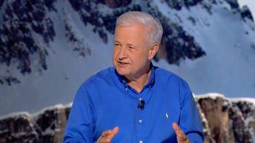 Portret Apoloniusza Tajnera w niebieskiej koszuli, z zaśnieżonymi g&oacute;rami w tle.