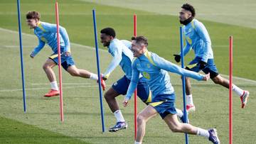 Piłkarze FC Barcelony wykonujący ćwiczenia z tyczkami na boisku treningowym.