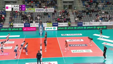 Rozgrywka siatk&oacute;wki kobiet na boisku. Zawodniczki w akcji, widoczna siatka, trybuny z kibicami oraz wynik meczu na telebimie.