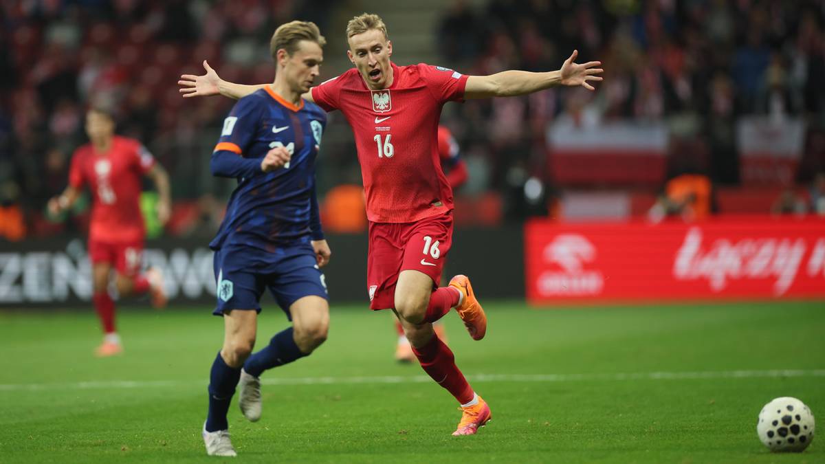 Dwóch piłkarzy walczy o piłkę na boisku, jeden w czerwonej koszulce Polski, drugi w niebieskiej