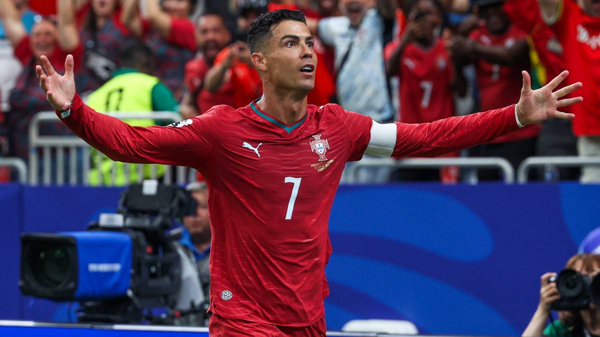 Cristiano Ronaldo w czerwonej koszulce reprezentacji Portugalii z numerem 7, biegnie po boisku z rozłożonymi rękami.