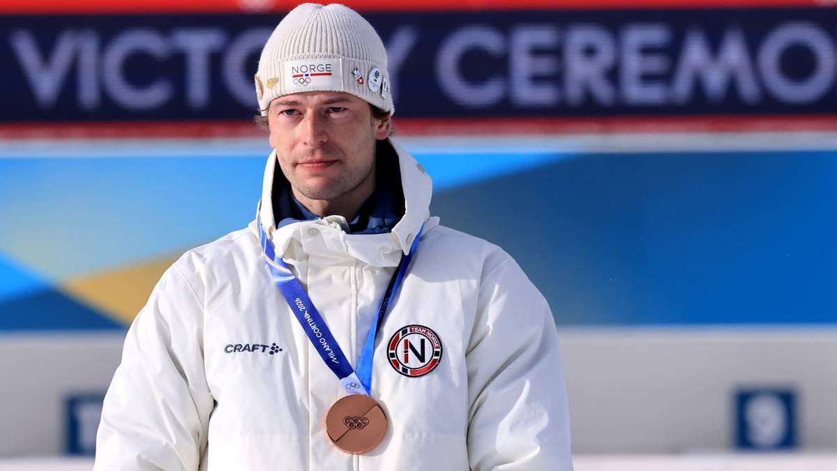 Portret mężczyzny w białej czapce i kurtce narciarskiej, na szyi wisi brązowy medal olimpijski.