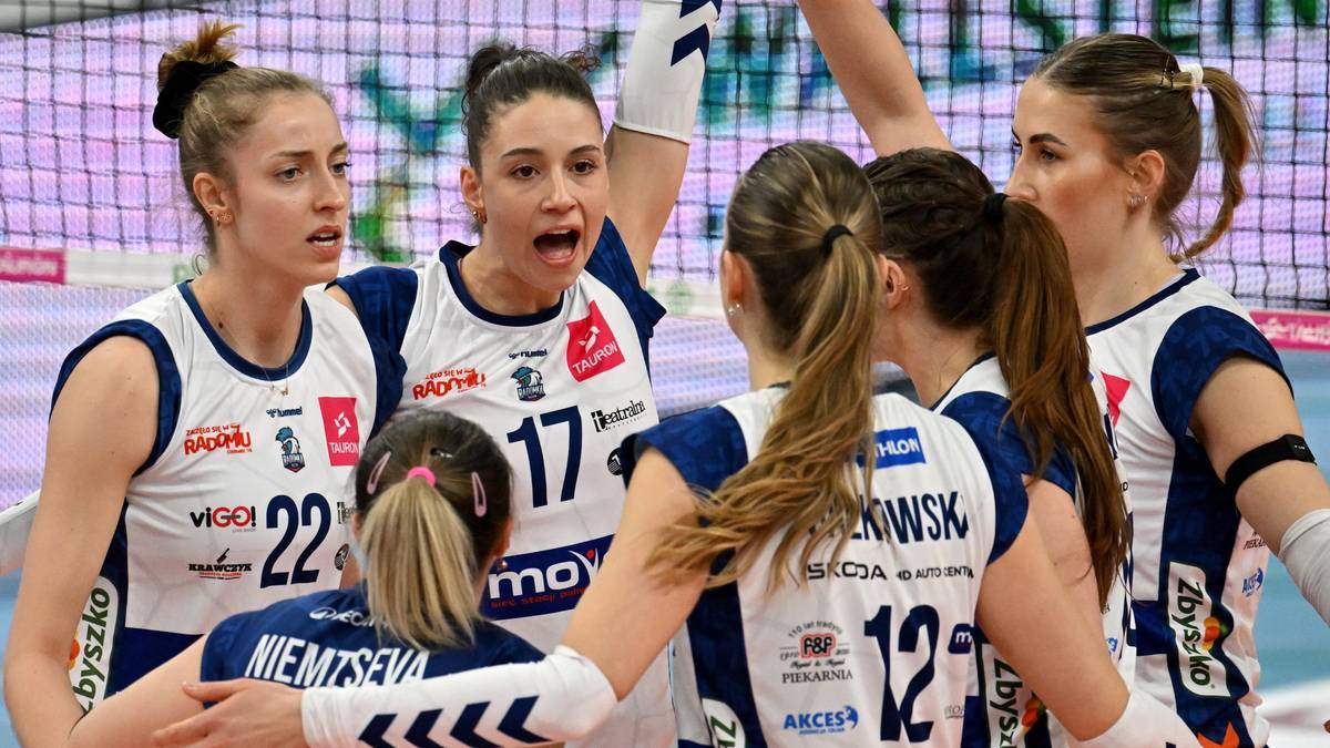 Grupa siatkarek w niebiesko-białych strojach sportowych świętujących lub rozmawiających po meczu.