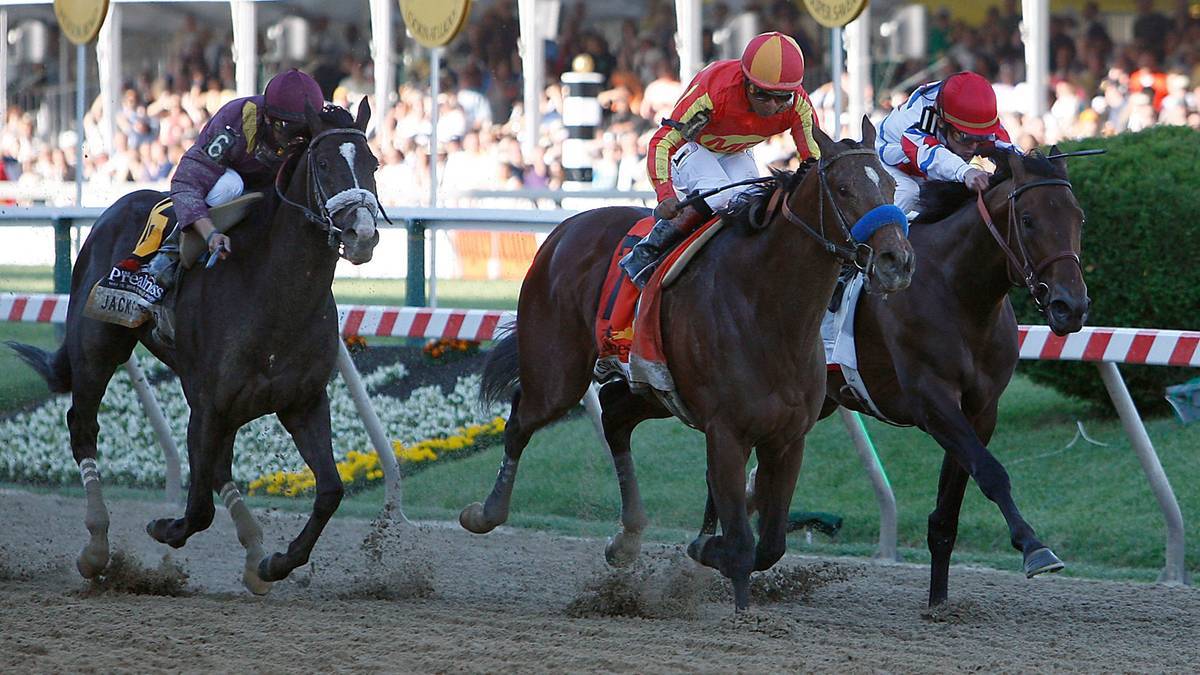 Trzy konie z dżokejami podczas wyścigu konnego na torze.