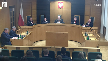 Pięciu sędzi&oacute;w w togach siedzi za stołem w sali rozpraw Trybunału Konstytucyjnego.