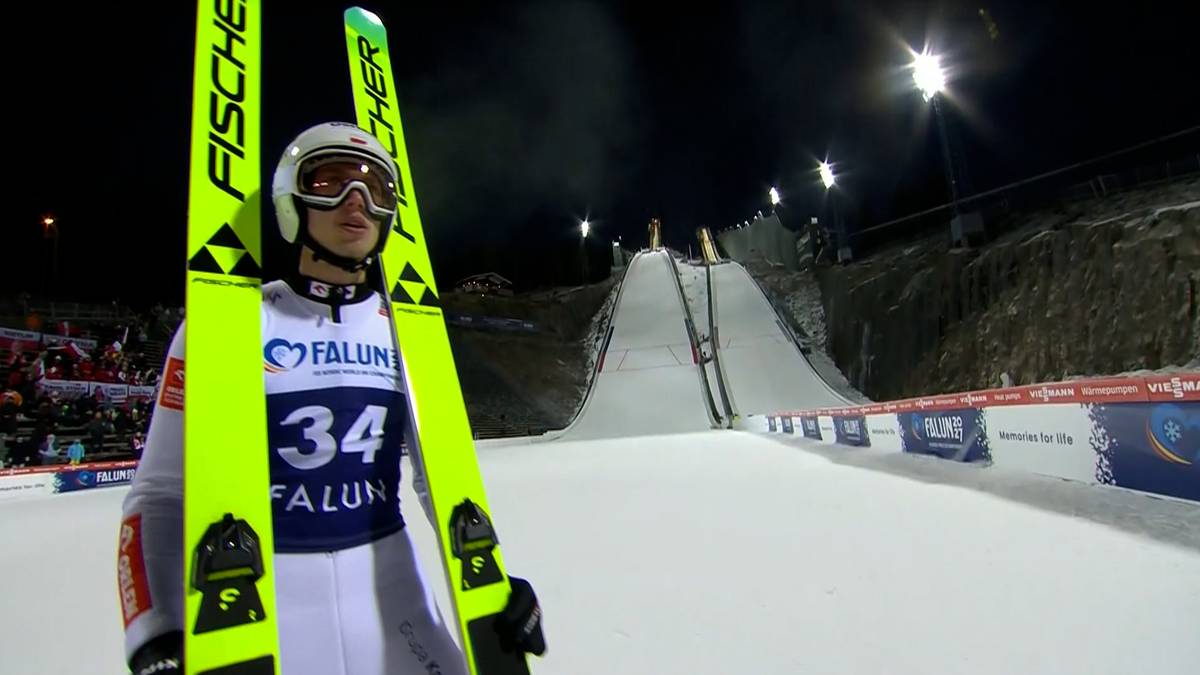 Skoczek narciarski w białym kombinezonie z neonowożółtymi nartami marki Fischer, przygotowuje się do skoku na skoczni narciarskiej w Falun. Widoczny numer 34 na nartach.