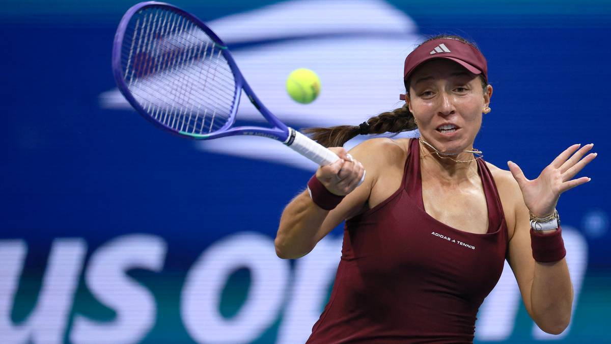Tenisistka w bordowym strojui czapce wykonuje dynamiczne uderzenie rakietą na korcie tenisowym, w tle widoczne jest logo US Open.