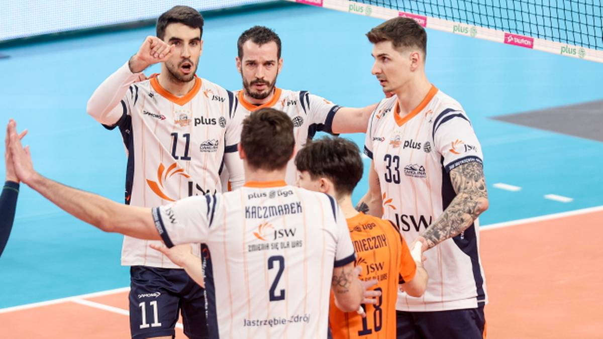 Czterech siatkarzy Jastrzębskiego Węgla w strojach sportowych, rozmawiających z młodszymi dziećmi w strojach pomarańczowych.