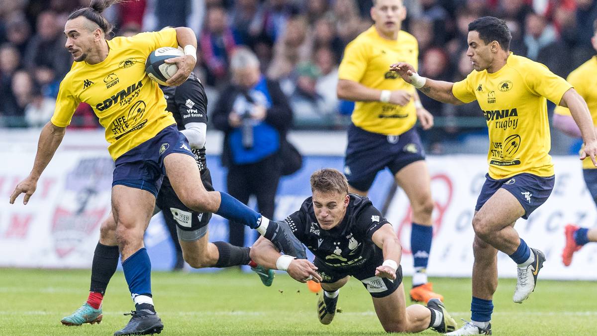 Trzech zawodników rugby w żółtych koszulkach walczy o piłkę, jeden z nich upada na ziemię.