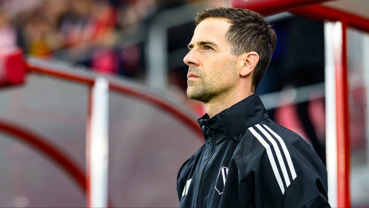 Trener siedzący na ławce rezerwowych, patrzący w bok.