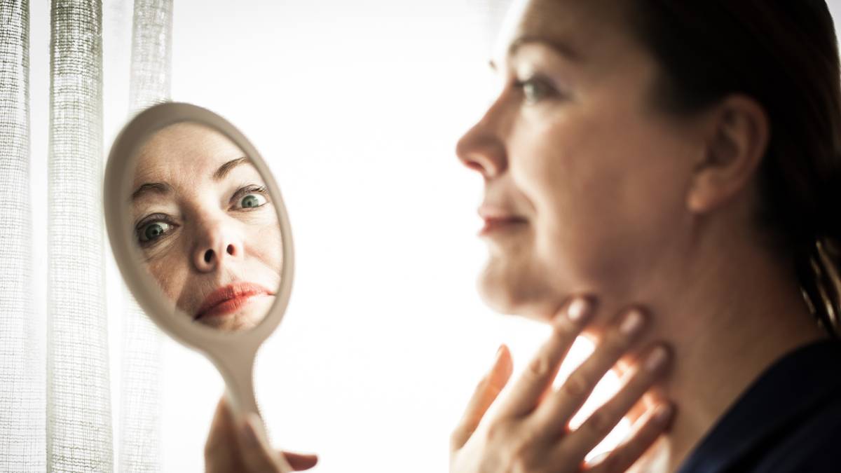 Kobieta patrzy w lusterko, w kt&oacute;rym odbija się jej zdeformowana twarz.