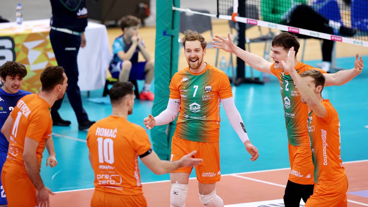 Siatkarze w pomarańczowych strojach świętują zwycięstwo na boisku siatkarskim.